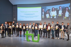 Eine Gruppe von Menschen mit Urkunden hinter dem TU-Logo bei der akademischen Jahresfeier der TU Dortmund.