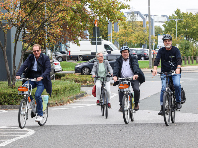 Vier Personen fahren mit Fahrrädern auf einer Straße. 
