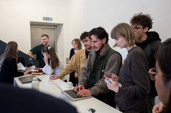 Several people stand at a counter and work together on laptops.