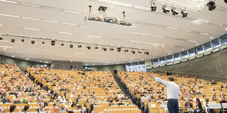 Ein Mann steht vor einem großem Publikum in einem Hörsaal.