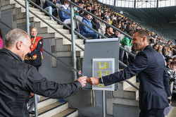 A man hands another man a dart in front of a stand filled with first-year students.