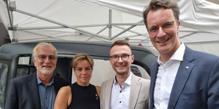 Gruppenfoto: Vier Personen vor einem kleinen Fahrzeug unter einem Pavillon.