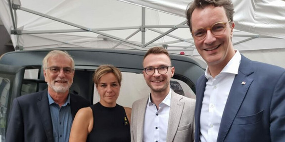 Gruppenfoto: Vier Personen vor einem kleinen Fahrzeug unter einem Pavillon.