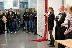 Foto: Eine Frau spricht vor mehreren Leuten in ein Mikrofon.