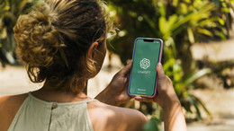 März Das Bild zeigt eine Frau von hinten mit einem Smartphone in der Hand auf dessen Bildschirm das Logo von ChatGPT zu sehen ist.