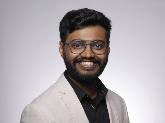 Porträtfoto von Hemanth Selva Raaja: Ein indischer Student mit Brille und Bart lächelt vor einem neutralen Hintergrund in die Kamera.