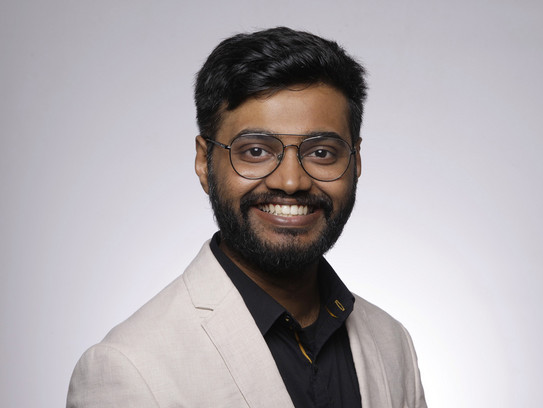 Porträtfoto von Hemanth Selva Raaja: Ein indischer Student mit Brille und Bart lächelt vor einem neutralen Hintergrund in die Kamera.
