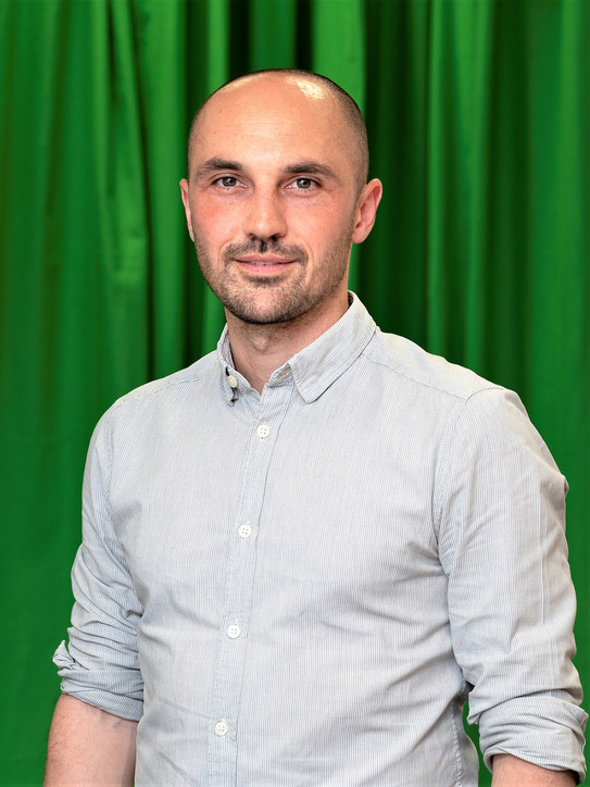 Portrait eines Mannes vor einem grünen Vorhang.