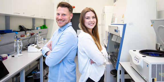Dr. Alexander Schenk und Julia Dreilich stehen Rücken an Rücken in einem Labor.
