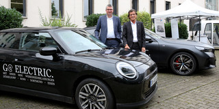 Zwei Männer stehen neben einem Auto, auf dem "Go Electric" steht.