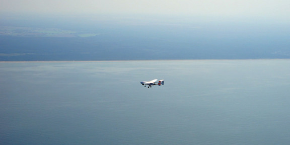 Starrflügelflugzeug A small plane flies over the sea.