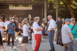 Besucher*innen eines Sommerfests sind draußen vor einer Bühne versammelt.