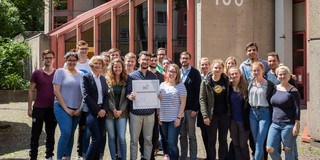 Gruppenfoto vor der Schule, einer hält eine Plakette in der Hand