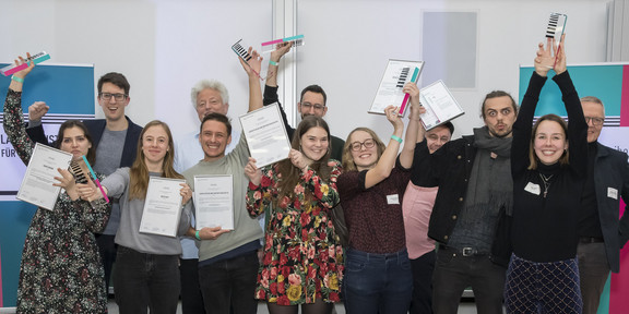 A group of young people beaming with joy holds up prizes and certificates