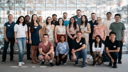 Eine Gruppenfoto internationaler Nachwuchswissenschaftler*innen vor einer Glaswand.