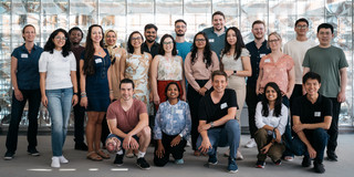 A group photo of international young scientists* in front of a glass wall.