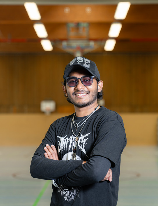 Porträtfoto von Sayed Atique Newaz: Sayed Atique Newaz trägt eine schwarze Kappe und getönte Brille. Er hat die Arme verschänkt und steht in einer Turnhalle.