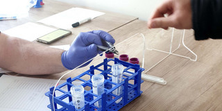 Several test tubes on a table, a person is handing over a test swab to another person.