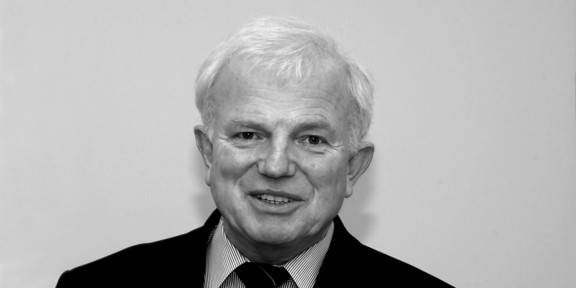 Black and white portrait of an older man in a suit smiling into the camera.