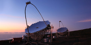 Zwei große Teleskope auf einer Bergkuppe vor einem Abendhimmel.
