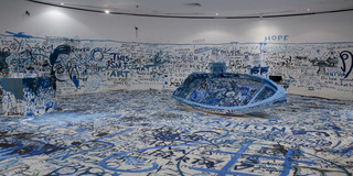 A large white room with blue words painted on the walls and the floor and a blue boat in the middle.
