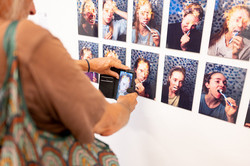 Eine Person steht vor acht Porträtfotos und zeigt auf eines dieser Fotos.