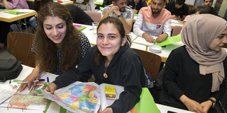 Three female students are sitting at a table in the seminar room. The student in the middle is holding a map of Germany in her hands. 