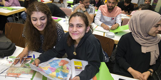 Drei Studentinnen sitzen an einem Tisch im Seminarraum. Die mittlere Studentin hält eine Deutschlandkarte in den Händen.