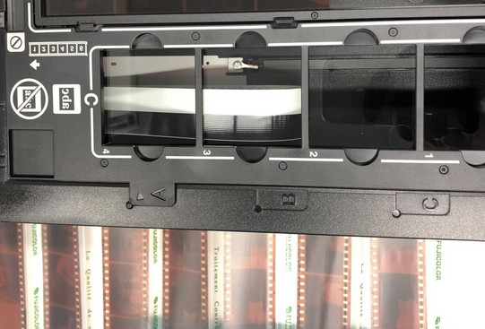 Black frames for photo negatives in front of an illuminated background. Two negatives are clamped in the upper frame.