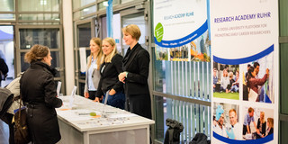 Three women stand behind and two women stand in front of an information booth.