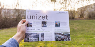 Zu sehen ist die unizet-Teitung der TU Dortmund. Sie wird ausgestreckt von einer Hand gehalten. Im Hintergrund sind eine Wiese und Bäume zu sehen.