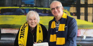 Zwei Männer mit BVB-Schals halten eine Urkunde in den Händen.