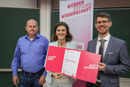 In the photo, you can see two men and a woman standing side by side, smiling at the camera for the picture.