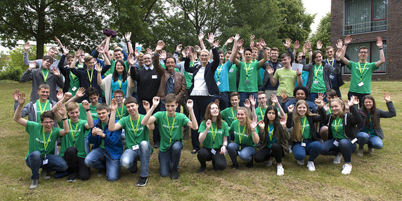 do-camp-ing Gruppenfoto auf einer Wiese mit Bäumen und einem Gebäude im Hintergrund.