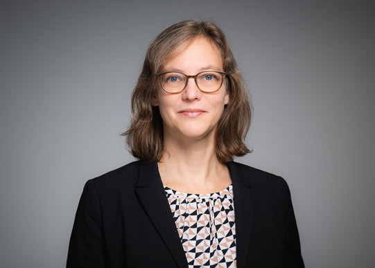 Portrait photo of Prof. Nele McElvany: Prof. McElvany is wearing a dark blazer and glasses. She stands in front of a gray background and smiles at the camera.