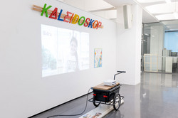 Ausstellung „Laufende Beobachtungen“ In einer Ausstellung steht ein Beamer vor einer weißen Wand. Es läuft ein Film.
