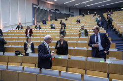 People stand at a distance in the rows of the Audimax and each hold a champagne glass in their hand