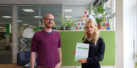 studium oecologicum Ein Mann steht neben einer Studentin, die ein Zertifikat in den Händen hält.