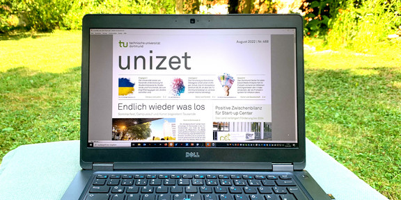 Ein Laptop steht auf einem Tisch, der auf einer Grünfläche am Campus der TU Dortmund aufgestellt wurde. Auf dem Monitor des Laptops ist ein Fenster mit einer Ausgabe der unizet geöffnet.