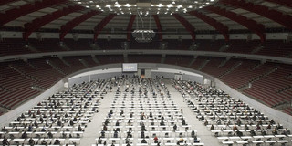 Blick von oben in eine Konzerthalle, in der viele Tische aufgebaut sind, an denen Personen sitzen.