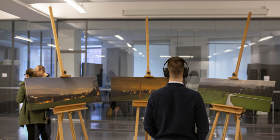 Eine Person trägt Kopfhörer und betrachtet drei Landschaftsbilder.