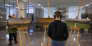 Eine Person trägt Kopfhörer und betrachtet drei Landschaftsbilder.