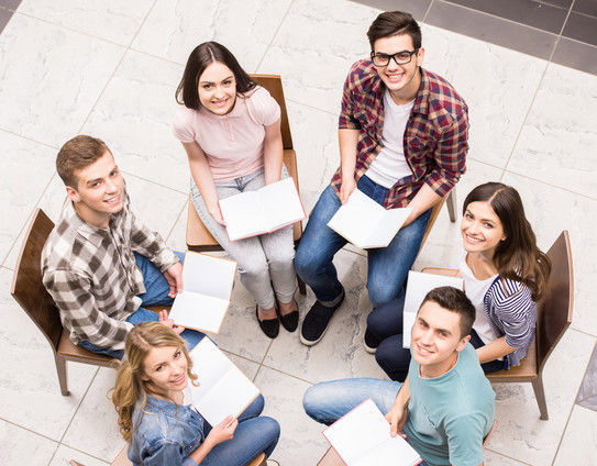 In einem Stuhlkreis sitzen sechs Student*innen und sie halten alle ein aufgeschlagenes Buch in der Hand