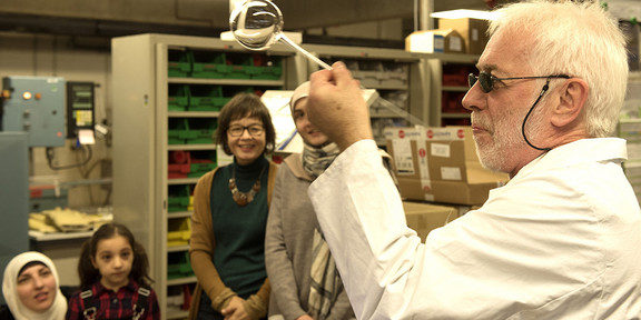 Ein Forscher in weißem Kittel hält ein Glasgefäß hoch. 
