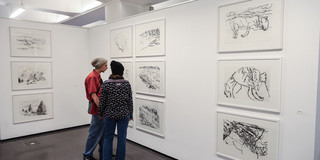 Two visitors look at the art paintings, which are all painted in black on a white background.