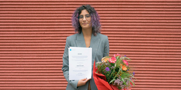 Leonor Cunha Leonor Cunha steht mit einer Urkunde und einem Blumenstrauß in der Hand vor einer roten Wand.