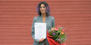 Leonor Cunha steht mit einer Urkunde und einem Blumenstrauß in der Hand vor einer roten Wand.