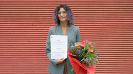 Leonor Cunha steht mit einer Urkunde und einem Blumenstrauß in der Hand vor einer roten Wand.