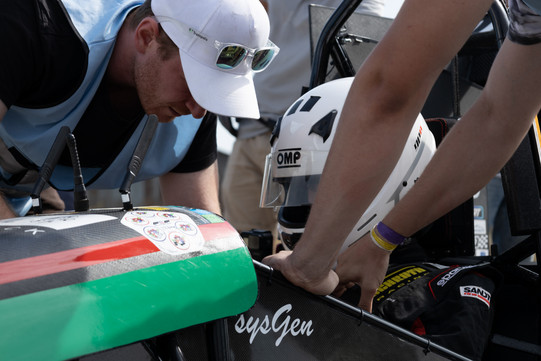 GET racing bei Formula Student France Eine Person mit Helm sitzt in einem Rennwagen. Zwei Personen beugen sich runter, um etwas zu besprechen.