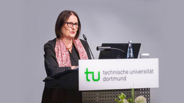 Juni Dr. Irina Scherbakowa hinter einem Rednerpult mit dem Logo der TU Dortmund. Der Hintergrund ist grau.